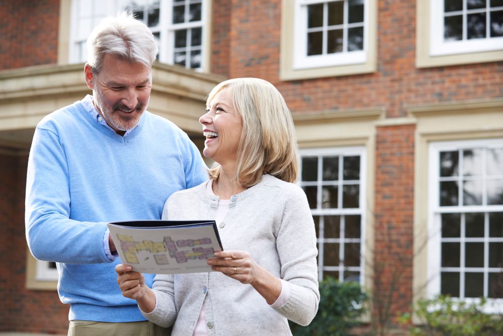 Residential Moving Services Estimate Image Smiling couple reviewing a floor plan outside their home, representing satisfied clients of residential moving services.